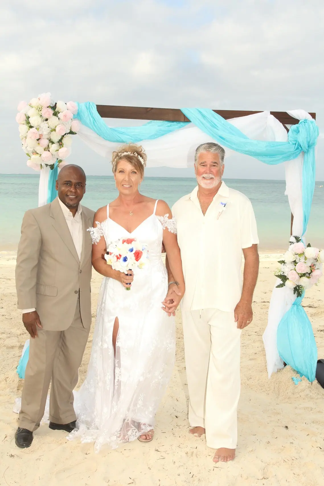 A couple with Antonio beneath a turquoise-draped arch