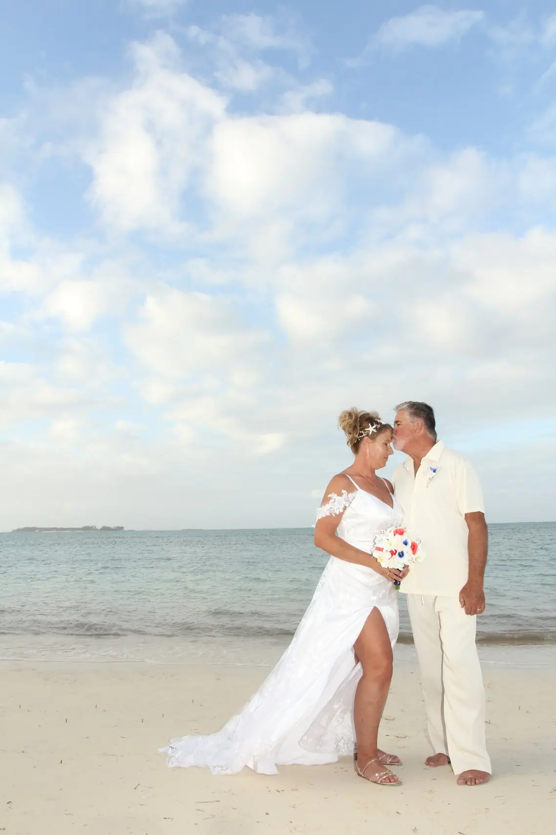 A couple share a kiss on the beach under a wide blue sky