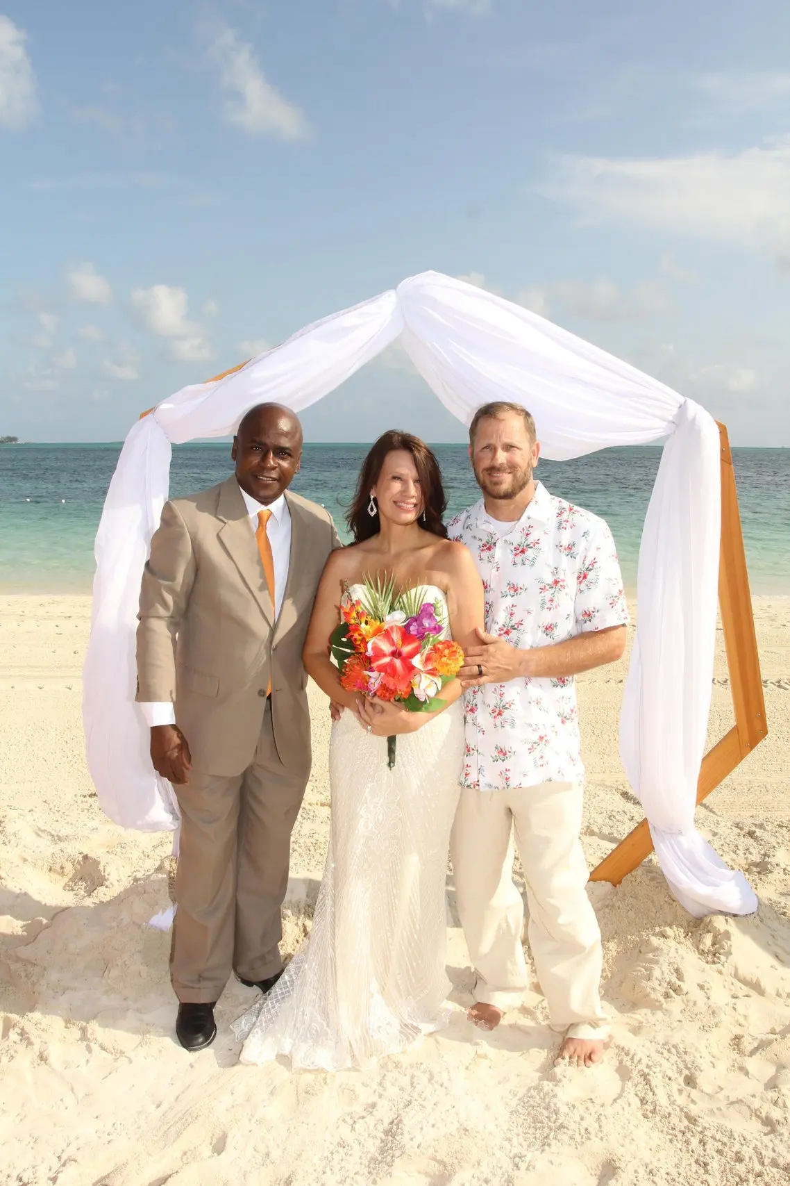 A couple with Antonio beneath a white draped arch on the sand
