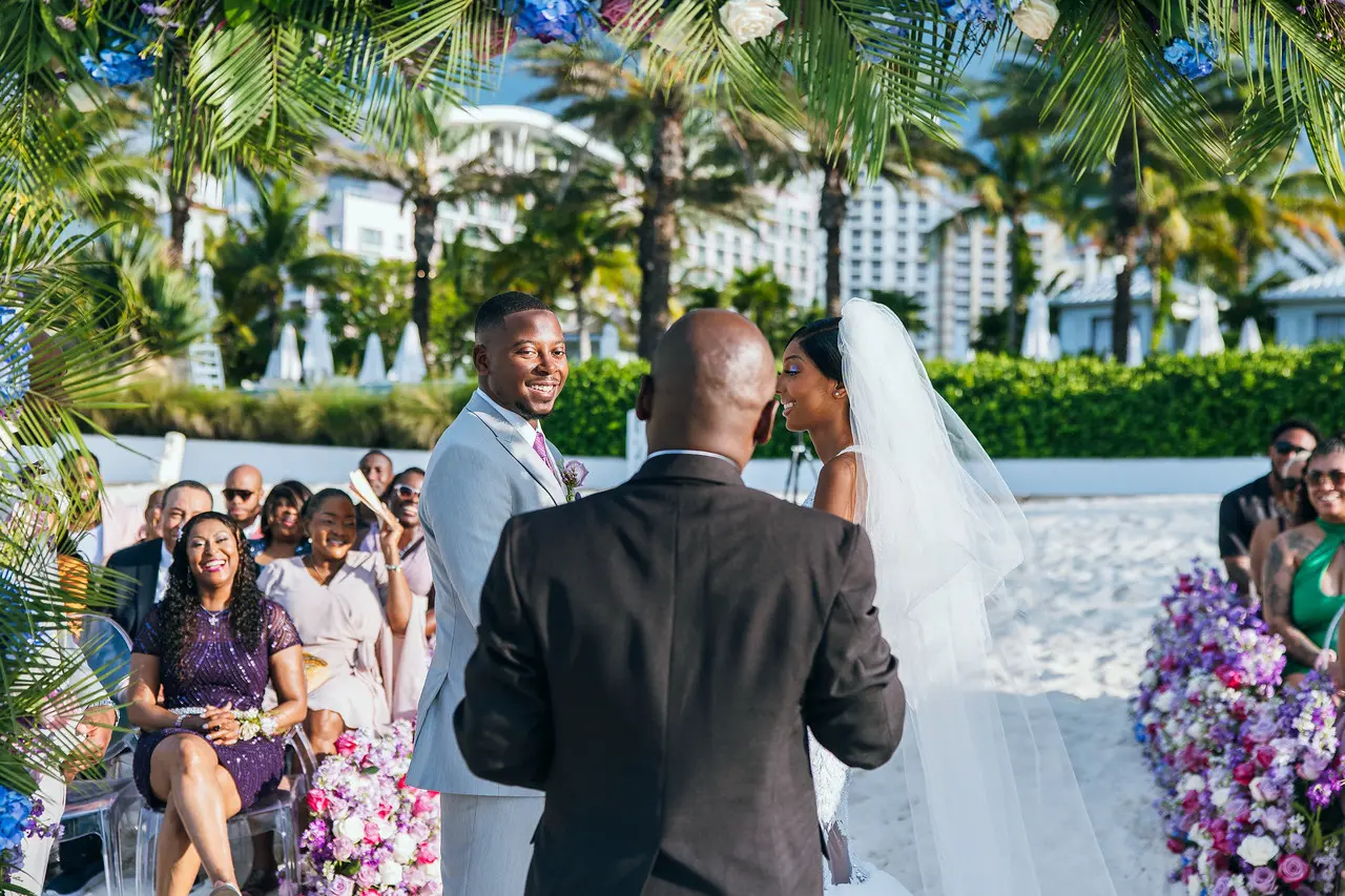 A beach ceremony at golden hour, guests seated, tiki torch lit